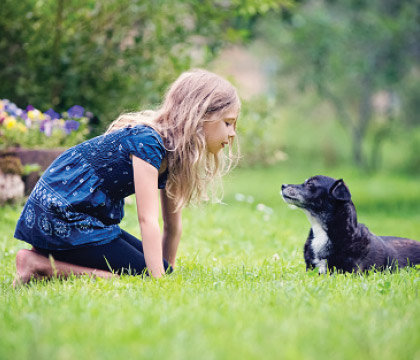 Young girl playing with dog in grassy yard