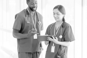 Male and female in scrubs standing and looking at tablet.