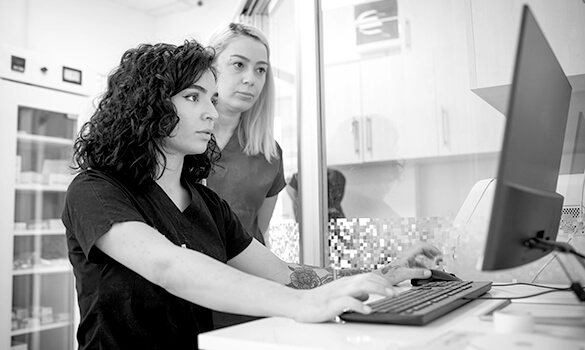 Black and white image of two female technicians looking at desktop computer.