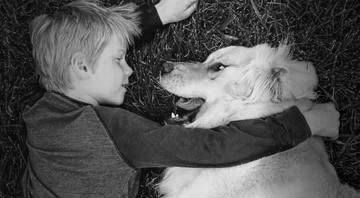 Child laying on grass with golden retriever.