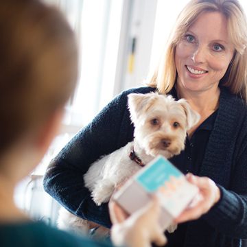 Woman holding dog gives FecalChek Home Collection Kit to veterinarian