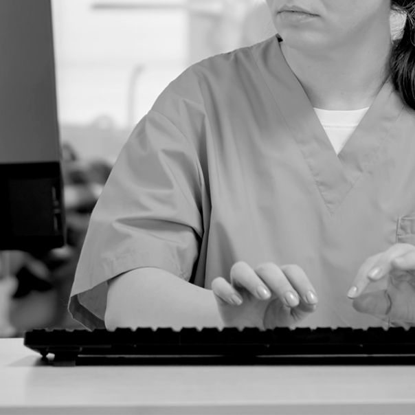 Female in scrubs typing at keyboard.